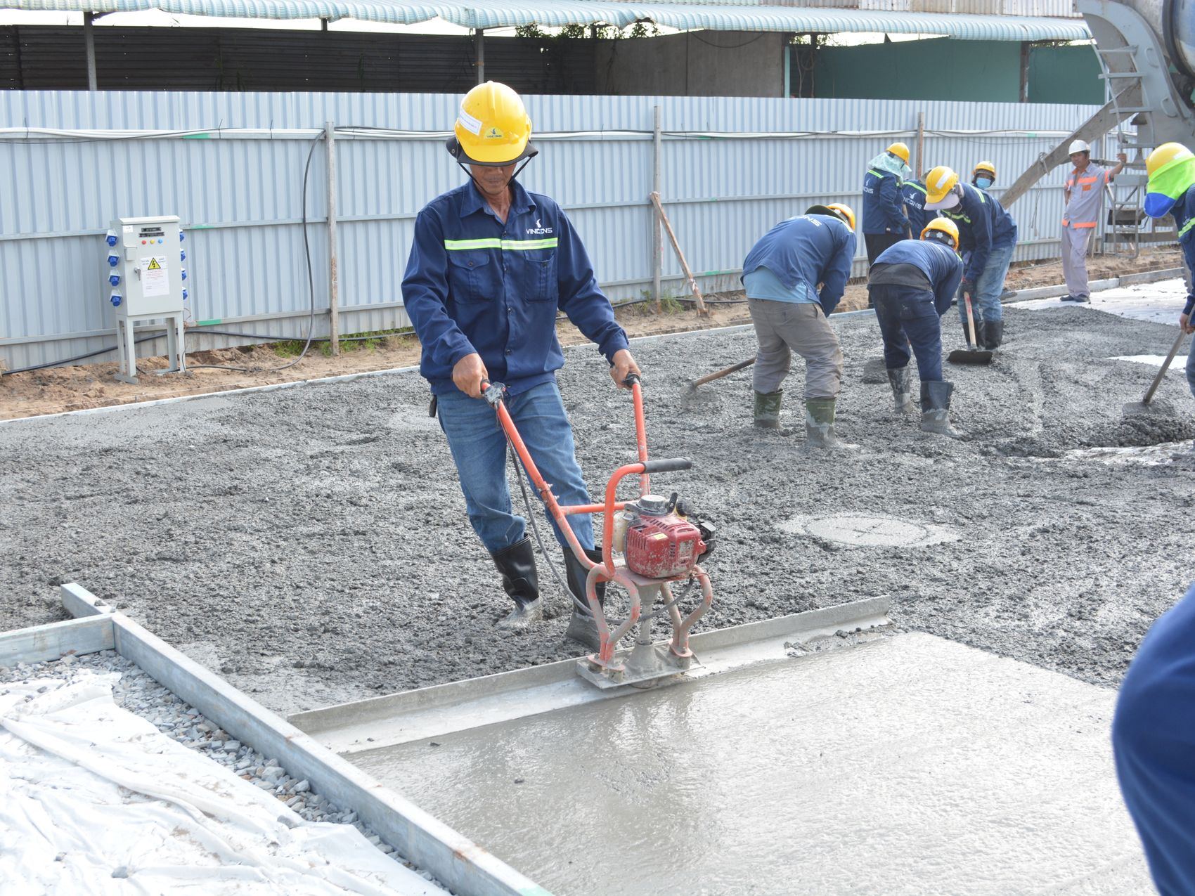 A team of workers uses a long straightedge tool to level wet concrete at a construction site.