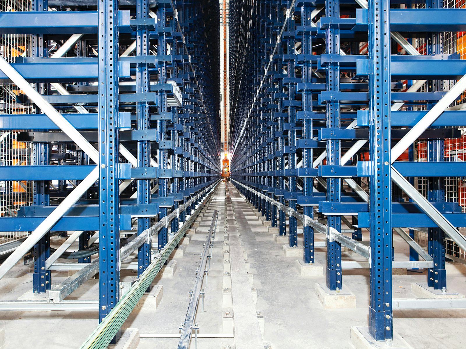 Long warehouse aisle between tall blue racking with a light resin floor