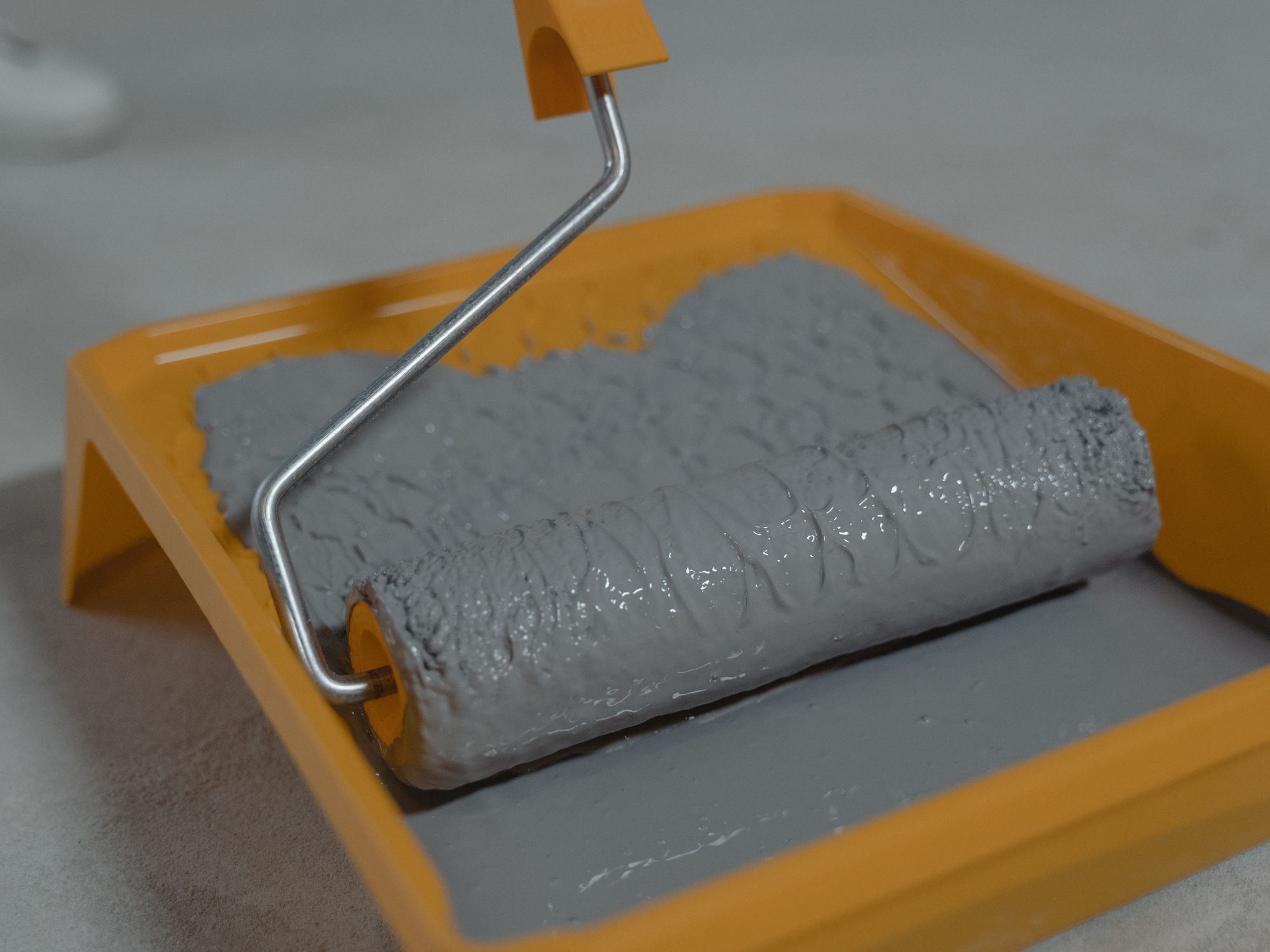 Grey paint roller loaded with coating sitting in an orange tray