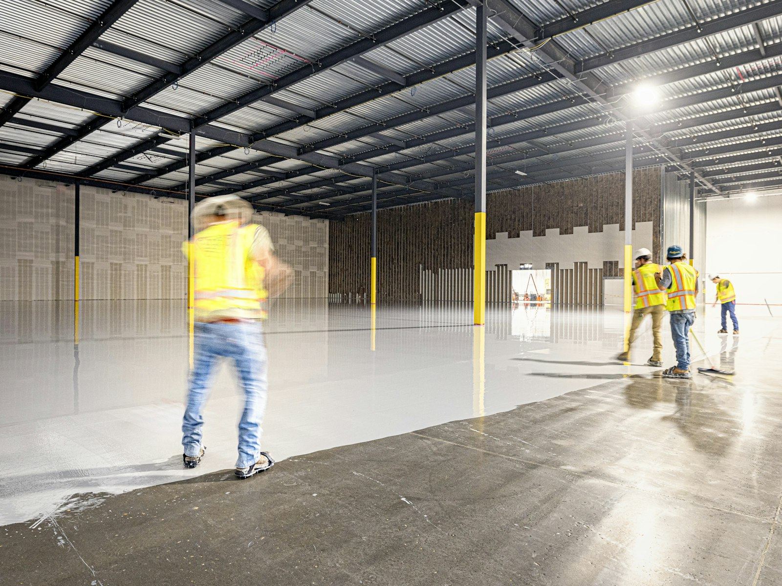 Workers in high-vis applying resin coating in a warehouse, slightly blurred motion