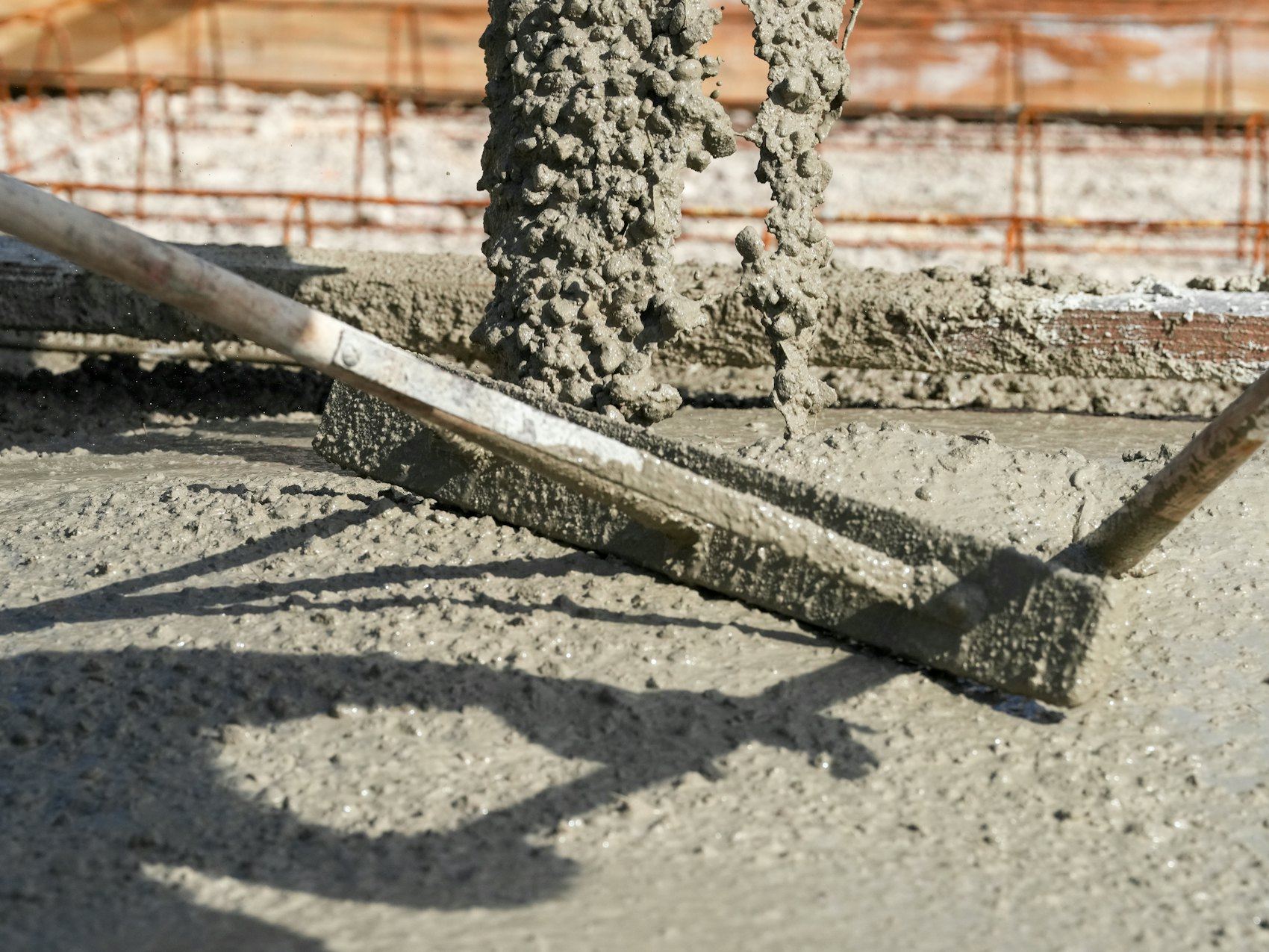 Two long trowels rest on a freshly leveled concrete surface with exposed rebar.