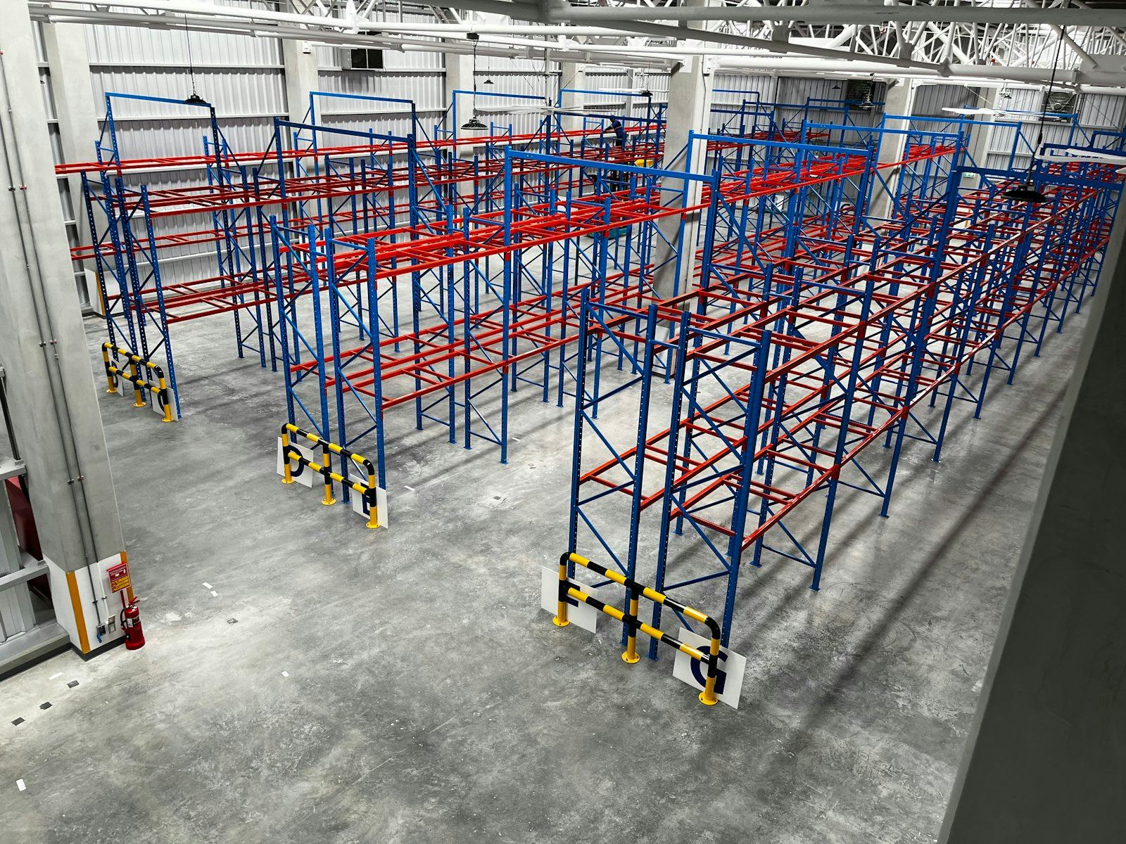 Empty warehouse with blue and red racking on a grey concrete floor