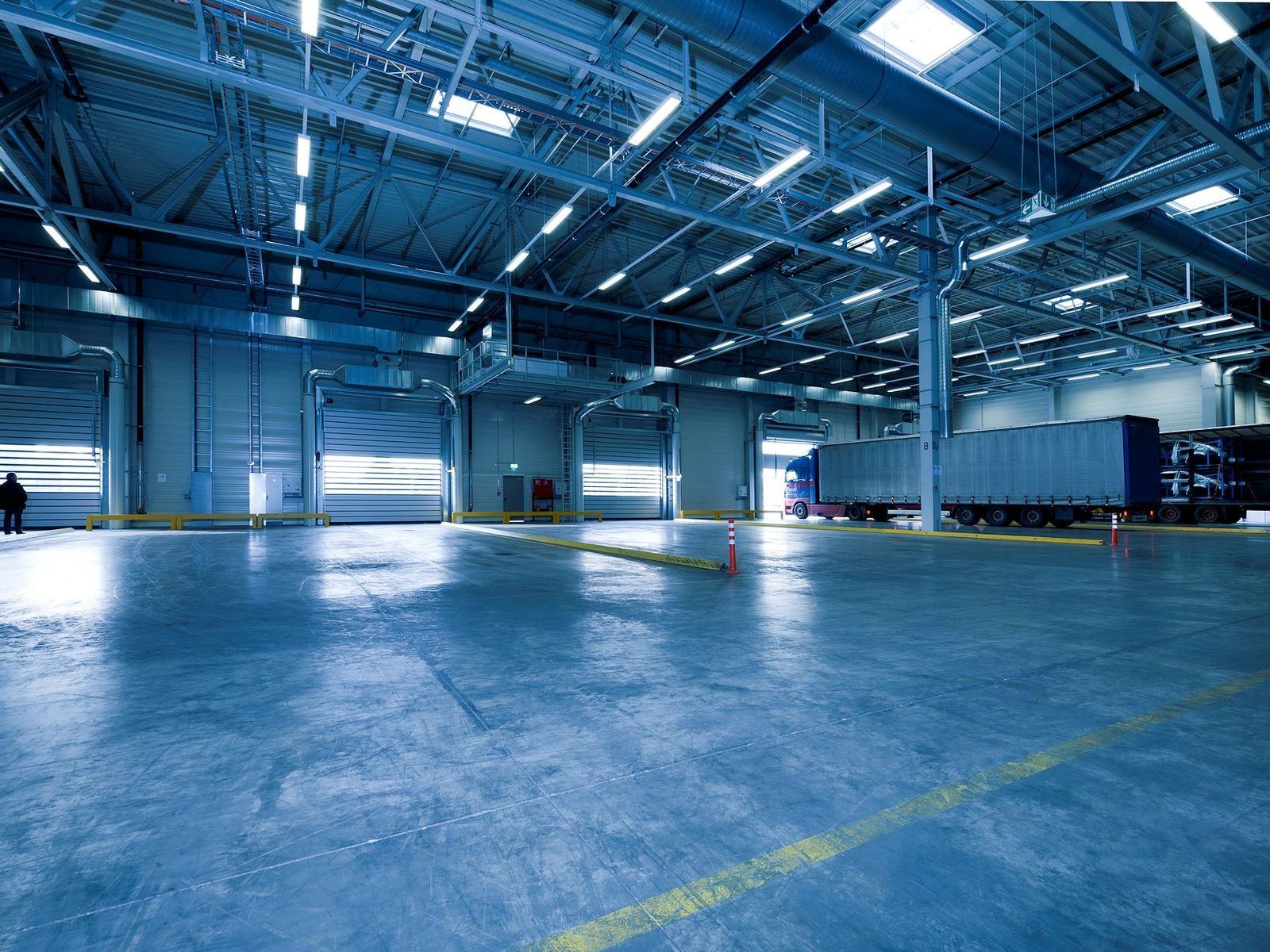 Large warehouse interior with open roller shutters and parked trucks