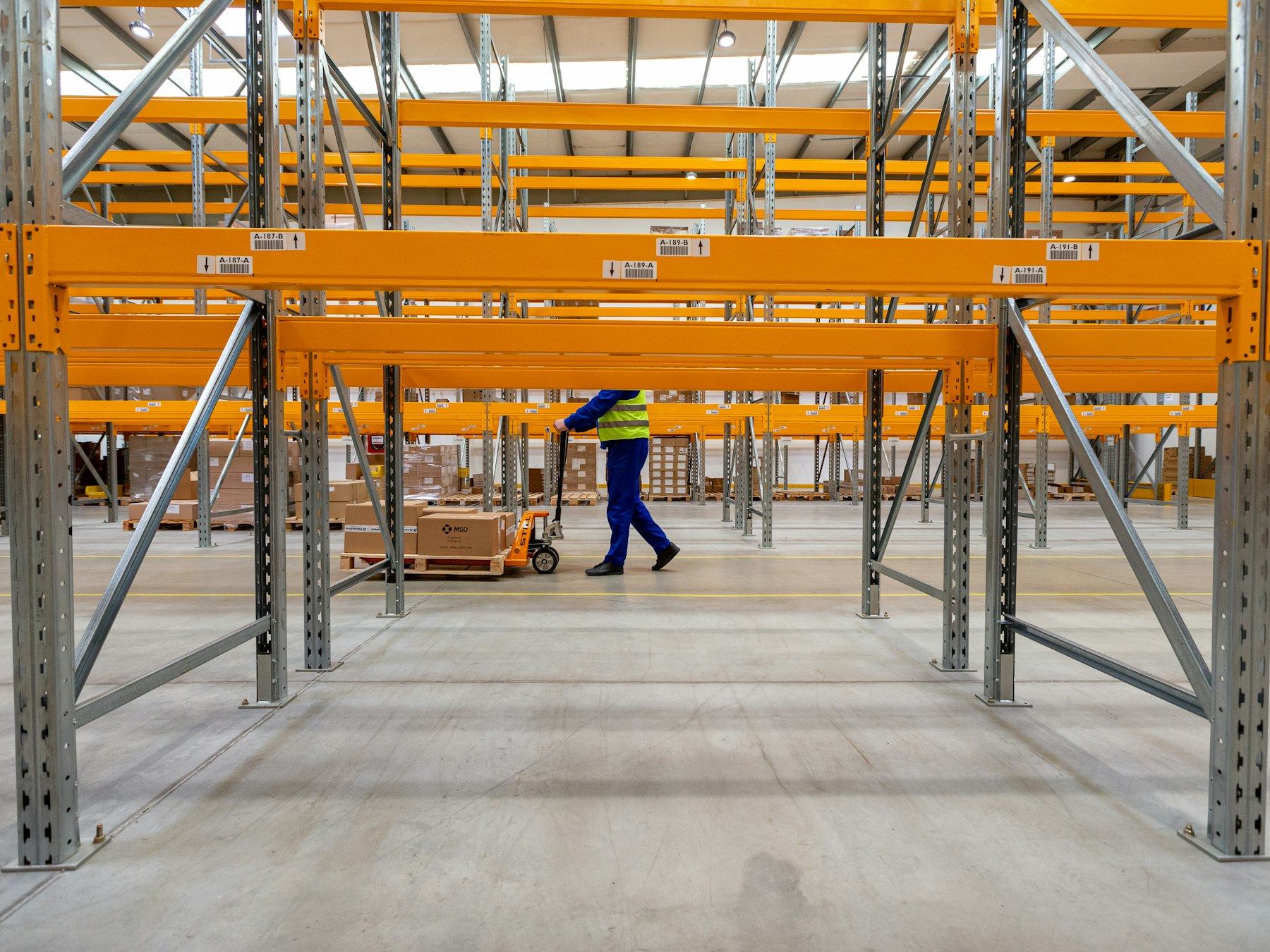 Worker in hi-vis walking a pallet truck between orange warehouse racking